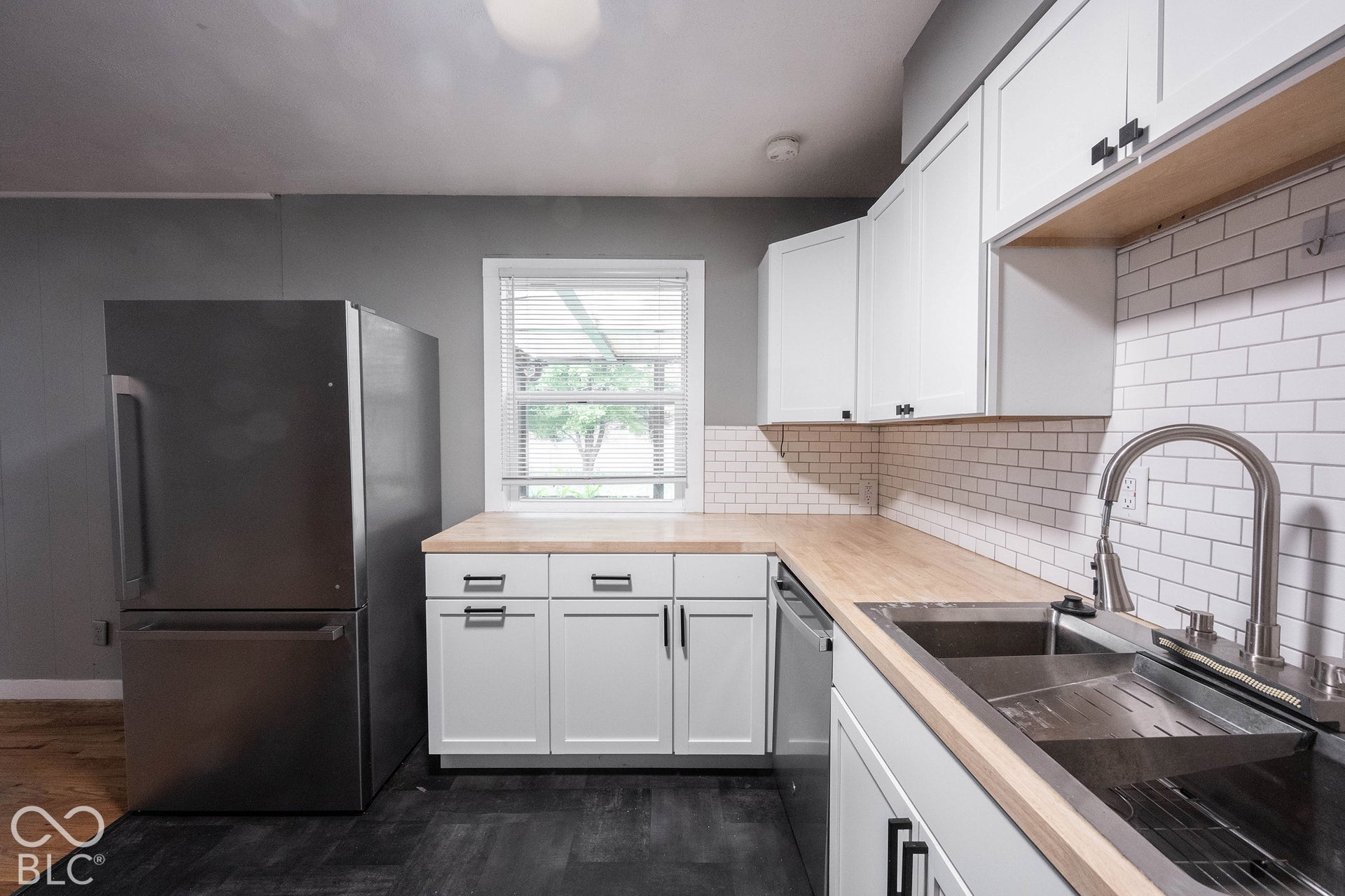 Kitchen featuring white shaker-style cabinetry, wood-finish countertops, subway tile backsplash, stainless steel appliances, and a dual-basin undermount sink with a high-arch faucet