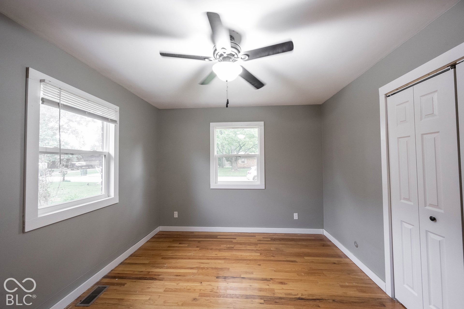 Room featuring wood-finish flooring, dual windows, ceiling fan, and bi-fold closet doors