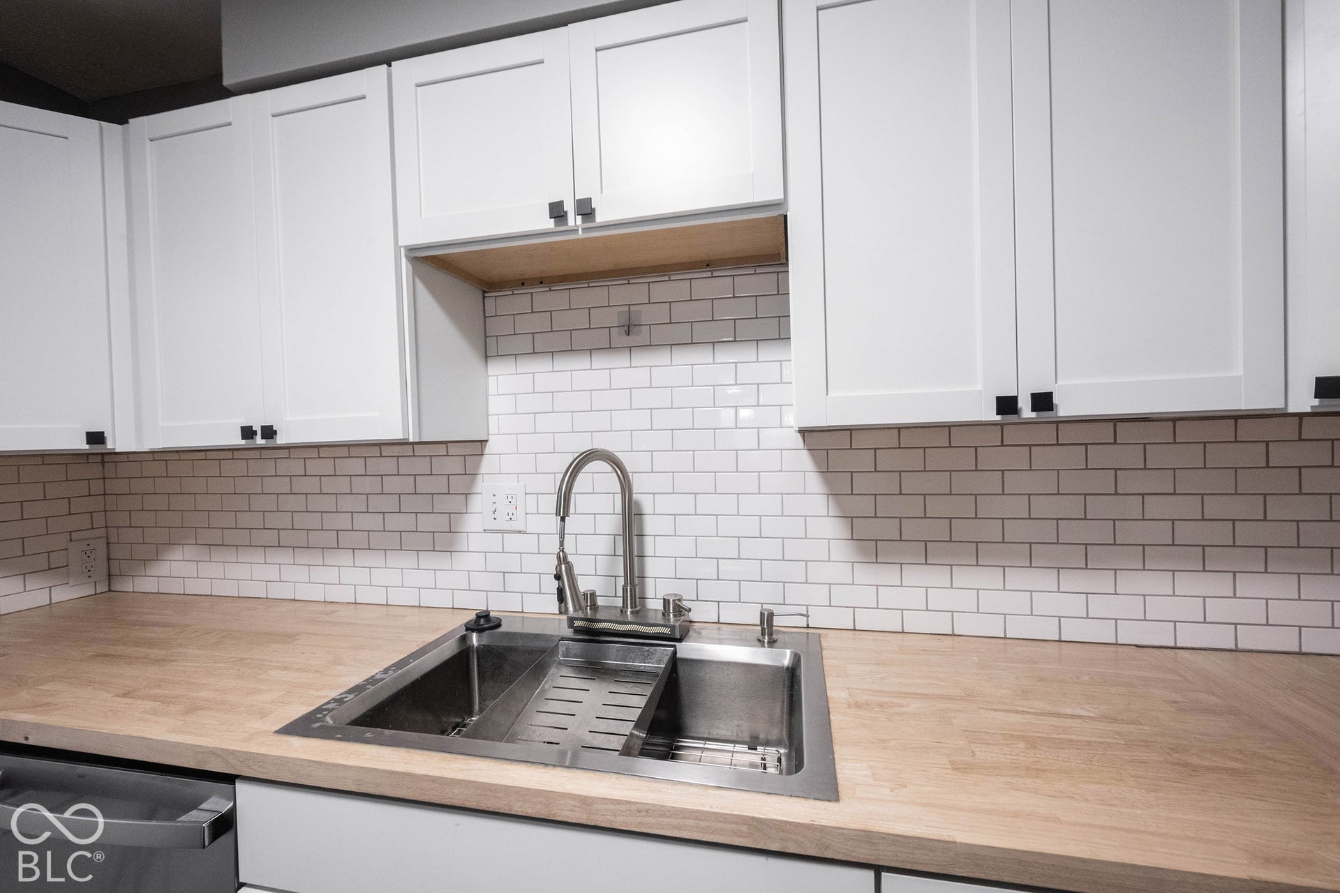 Kitchen featuring white shaker-style cabinetry, wood-finish countertops, subway tile backsplash, stainless steel drop-in sink, and a high-arch pull-down faucet