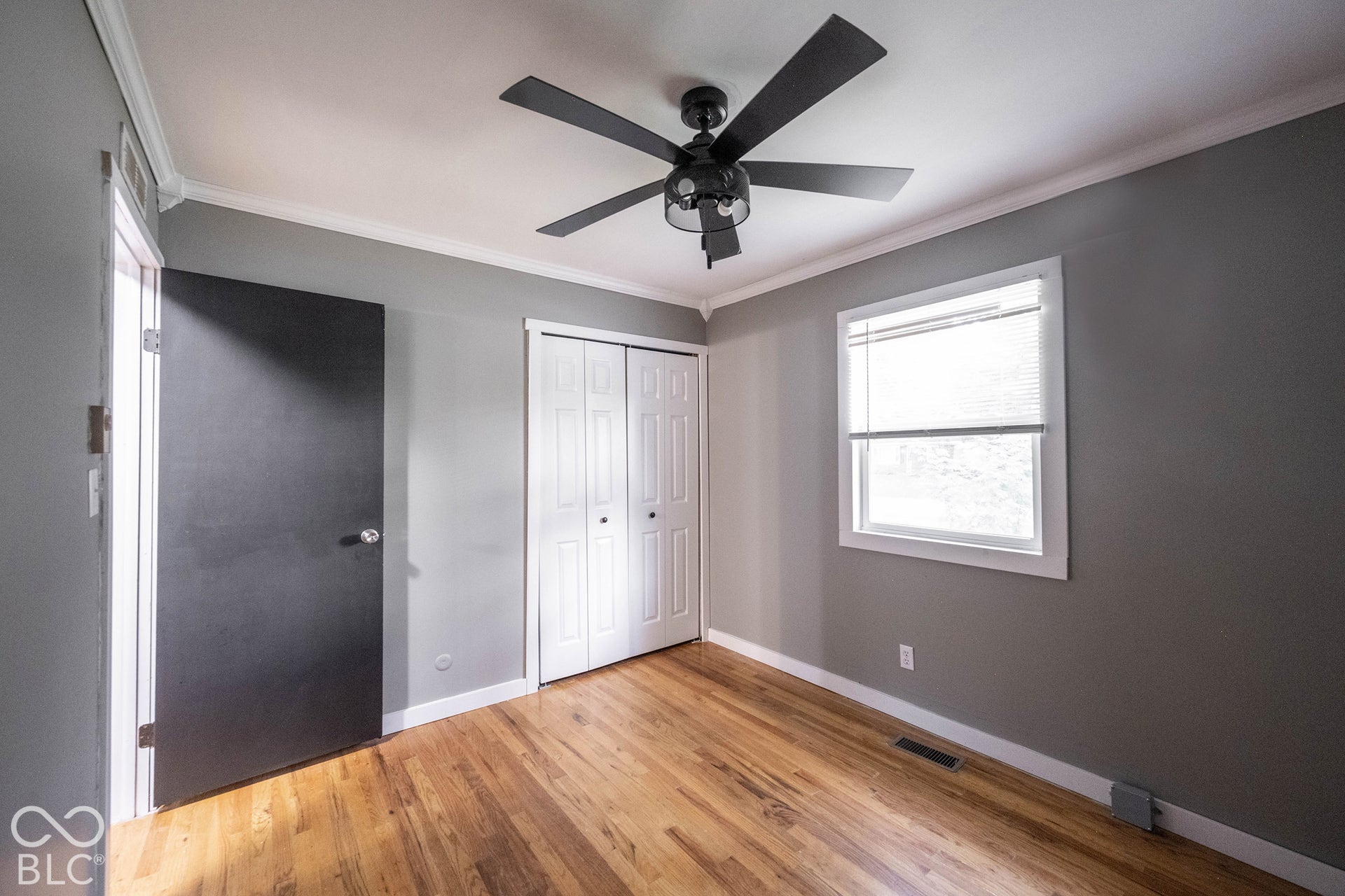 Room featuring wood-finish flooring, a matte black multi-blade ceiling fan, white bi-fold closet doors, and crown molding