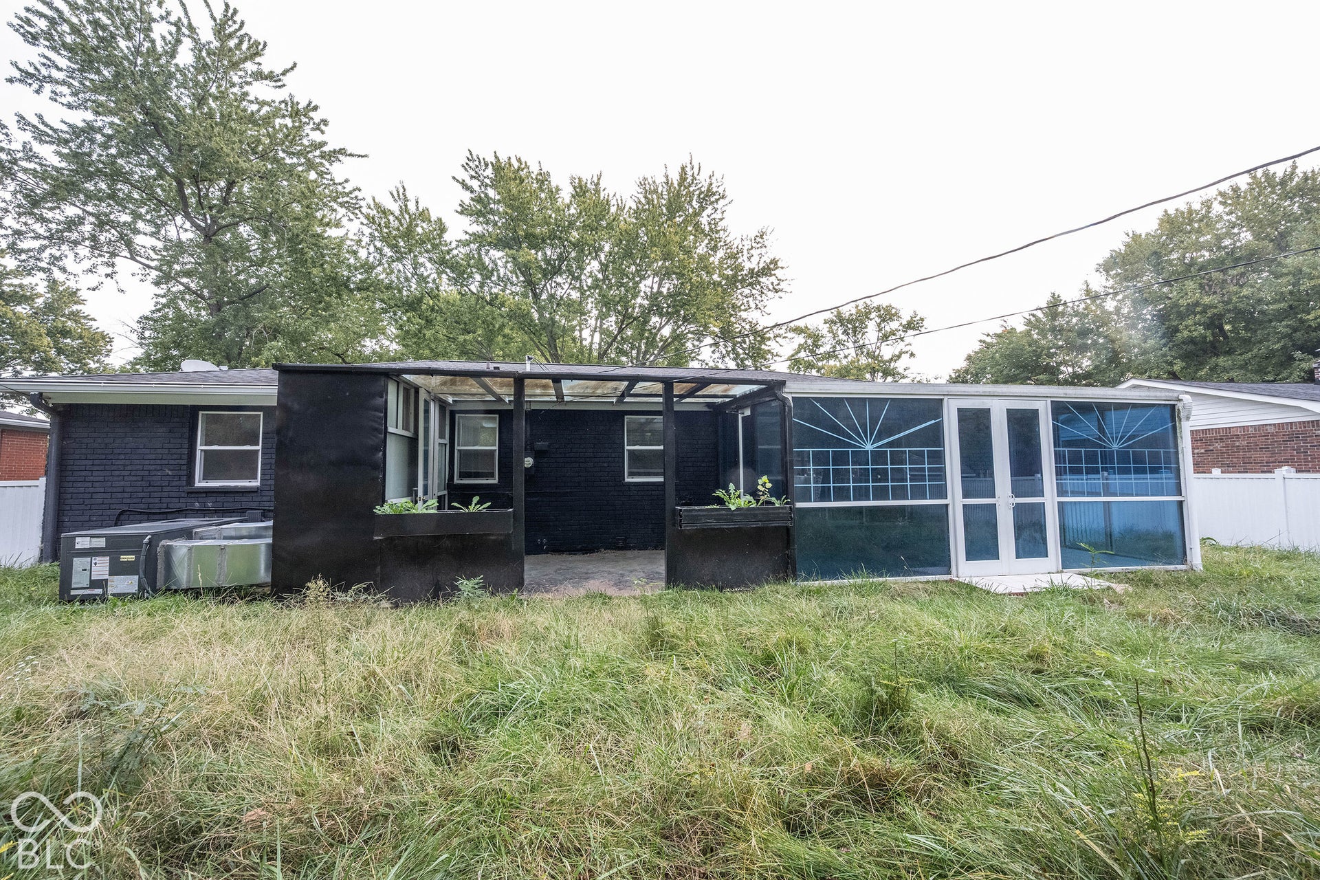 Rear exterior featuring a black-painted masonry finish, a covered patio area with integrated planter boxes, and an enclosed sunroom with decorative screen panels