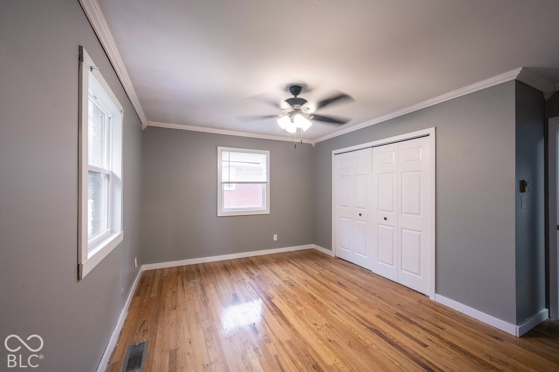 Wood-finish flooring, neutral wall tones, crown molding, multi-panel bifold closet doors, and a ceiling-mounted light fixture with fan