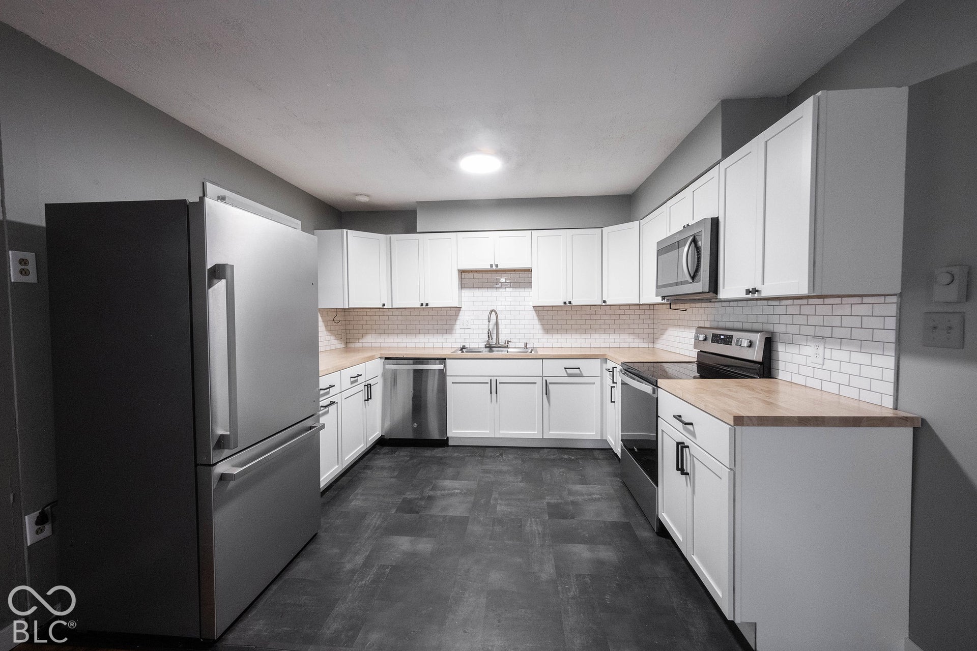 Kitchen featuring white cabinetry, wood countertops, a subway tile backsplash, stainless steel appliances, and dark tile flooring