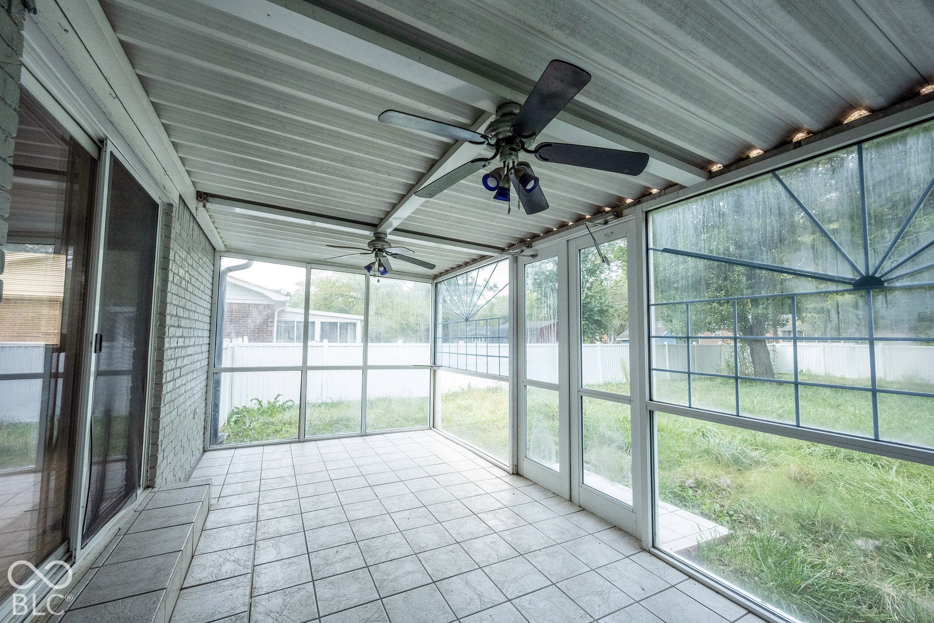 Screened-in porch featuring tile flooring, a corrugated metal ceiling, dual ceiling fans, and floor-to-ceiling window panels