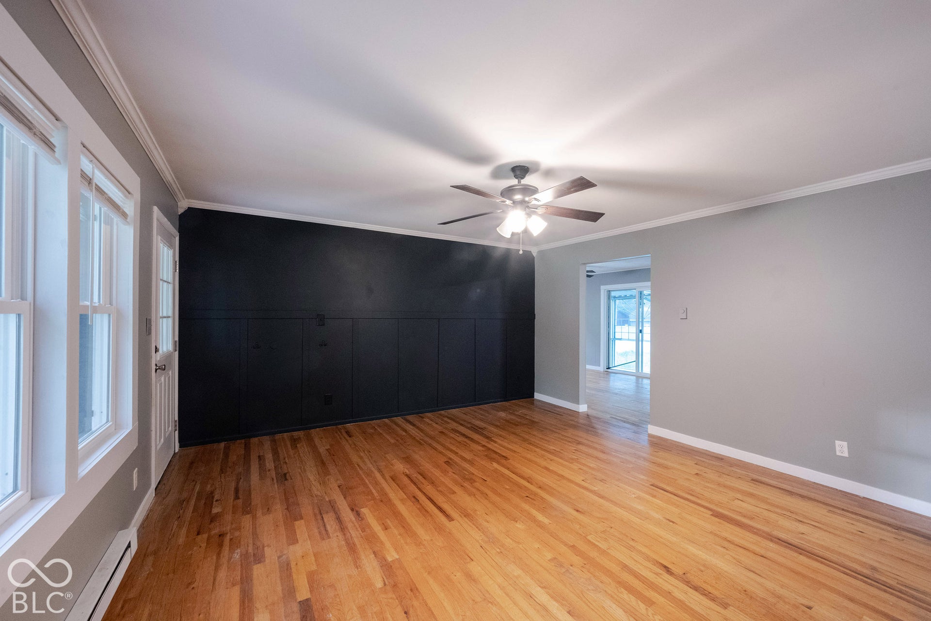 Room featuring wood-finish flooring, a matte black accent wall with vertical paneling, crown molding, and a multi-light ceiling fan