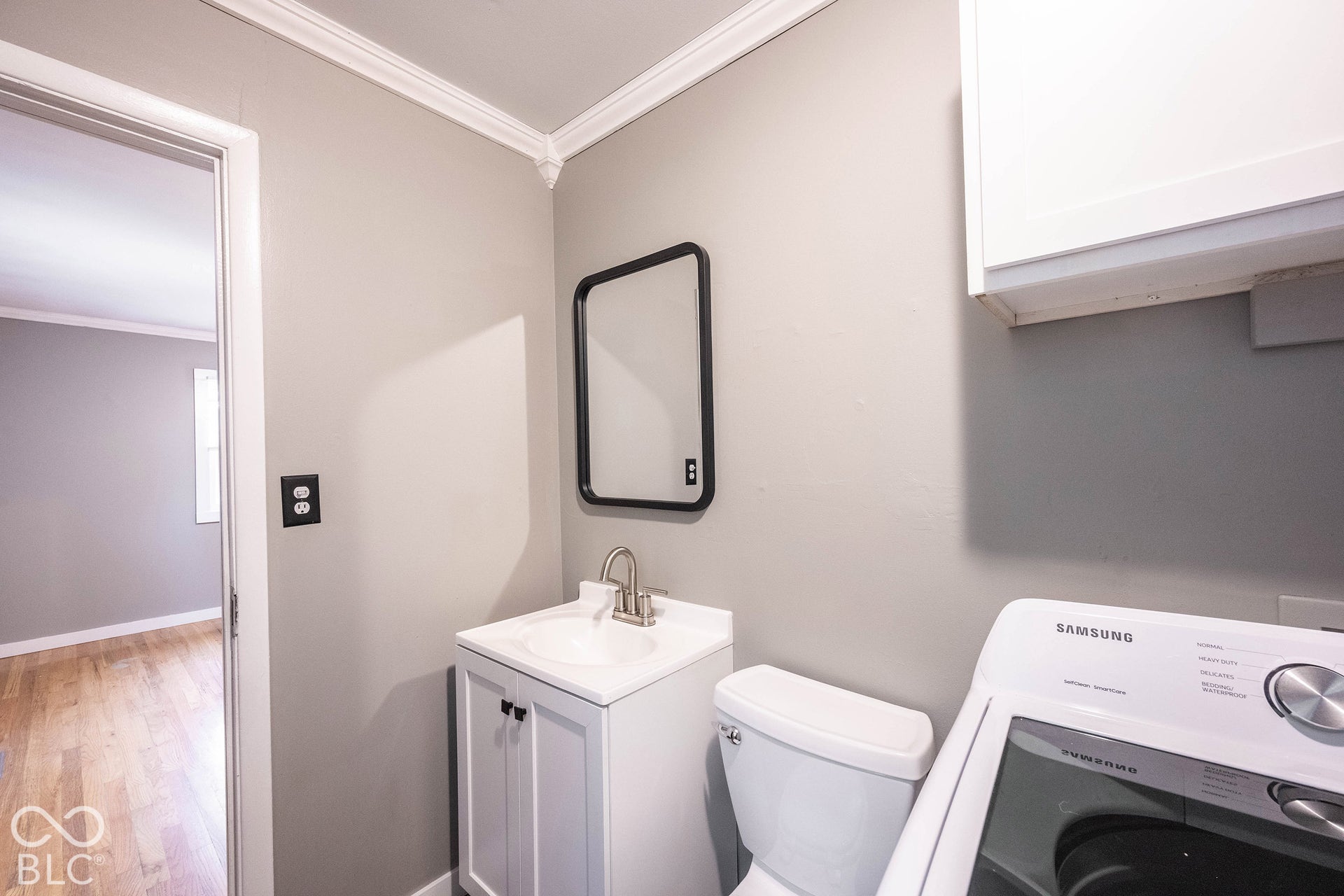 Utility space featuring a white vanity cabinet with an integrated sink, polished metal faucet, wall-mounted mirror with a black frame, and crown molding