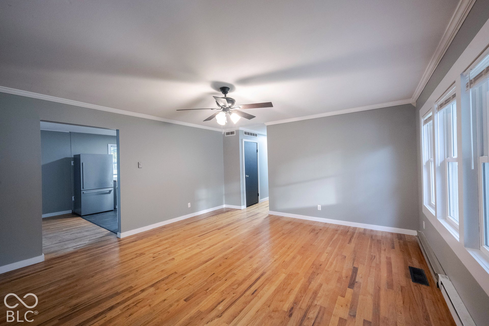 Living area featuring wood-finish flooring, crown molding, a central ceiling fan with integrated lighting, and multiple windows