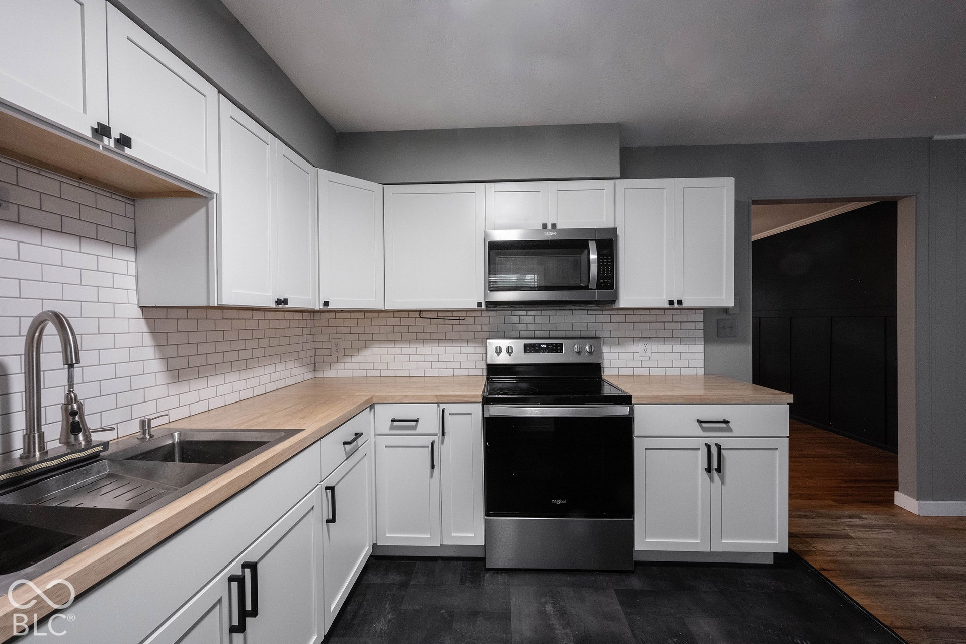 Kitchen featuring white shaker-style cabinetry, wood-finish countertops, stainless steel appliances, a white subway tile backsplash, and a stainless steel undermount sink with a high-arch faucet