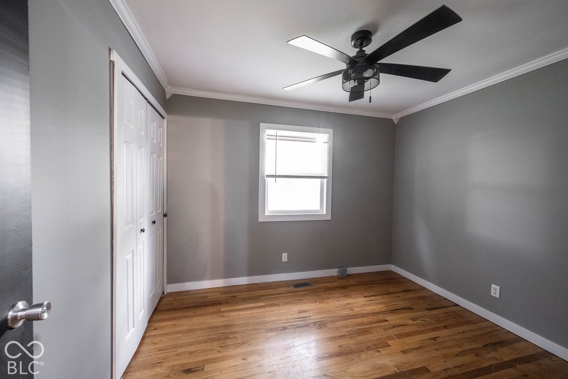 Room featuring wood-finish flooring, a matte black multi-blade ceiling fan, crown molding, and double-door closet cabinetry