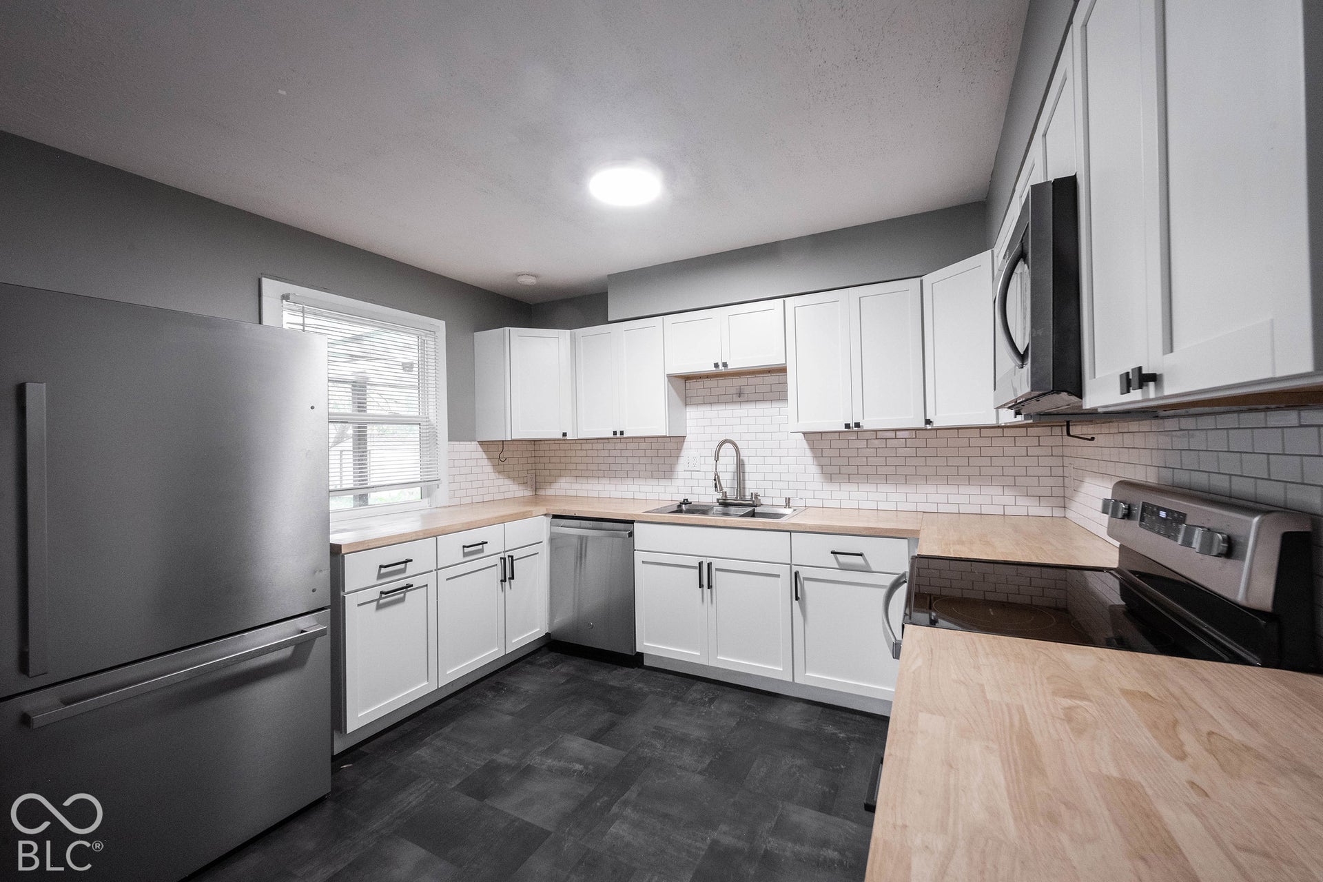 Kitchen featuring white shaker-style cabinetry, butcher block countertops, white subway tile backsplash, stainless steel appliances, and dark tile flooring