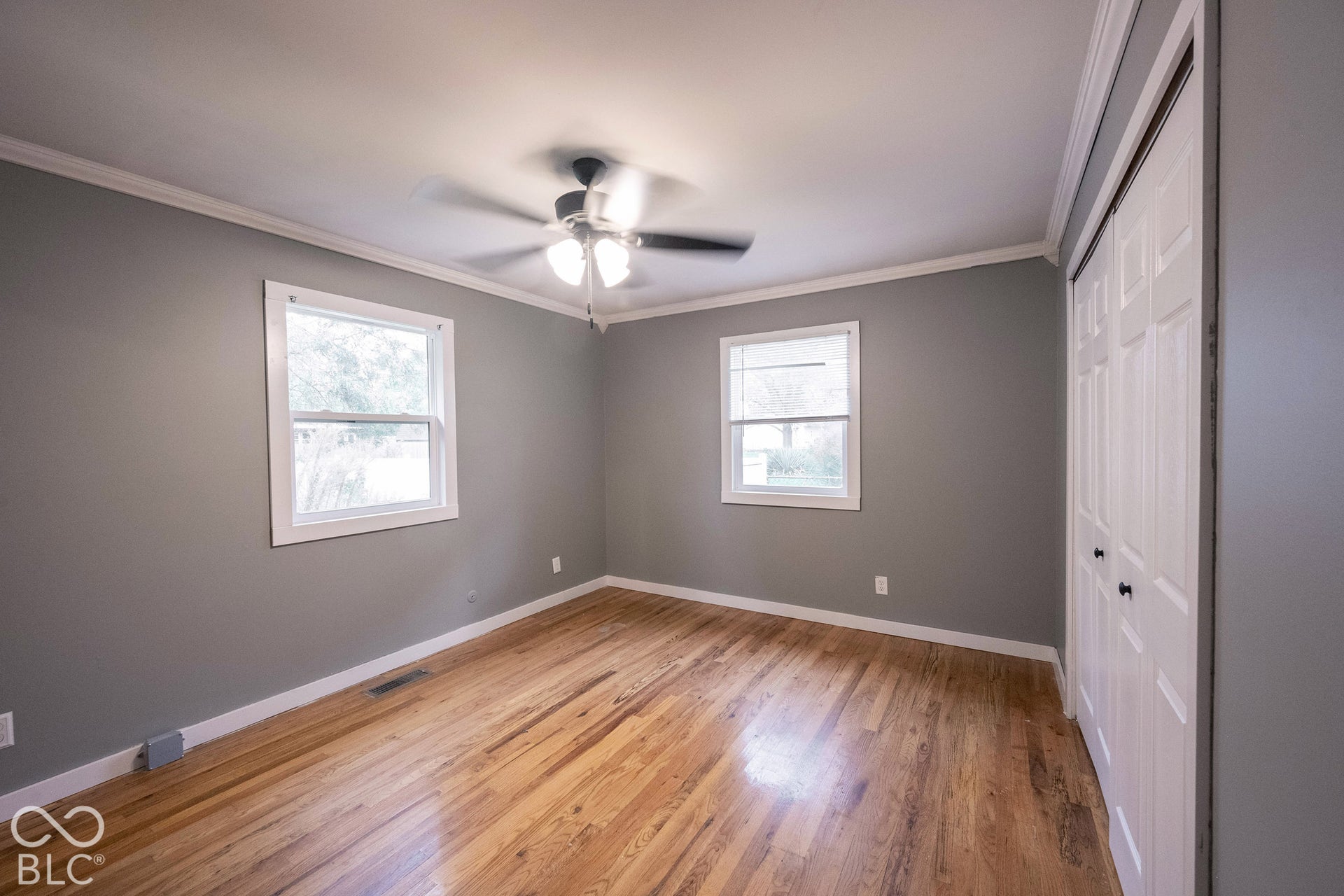 Room featuring wood-finish flooring, crown molding, dual-pane windows, a central ceiling fan with integrated lighting, and a closet with bifold doors