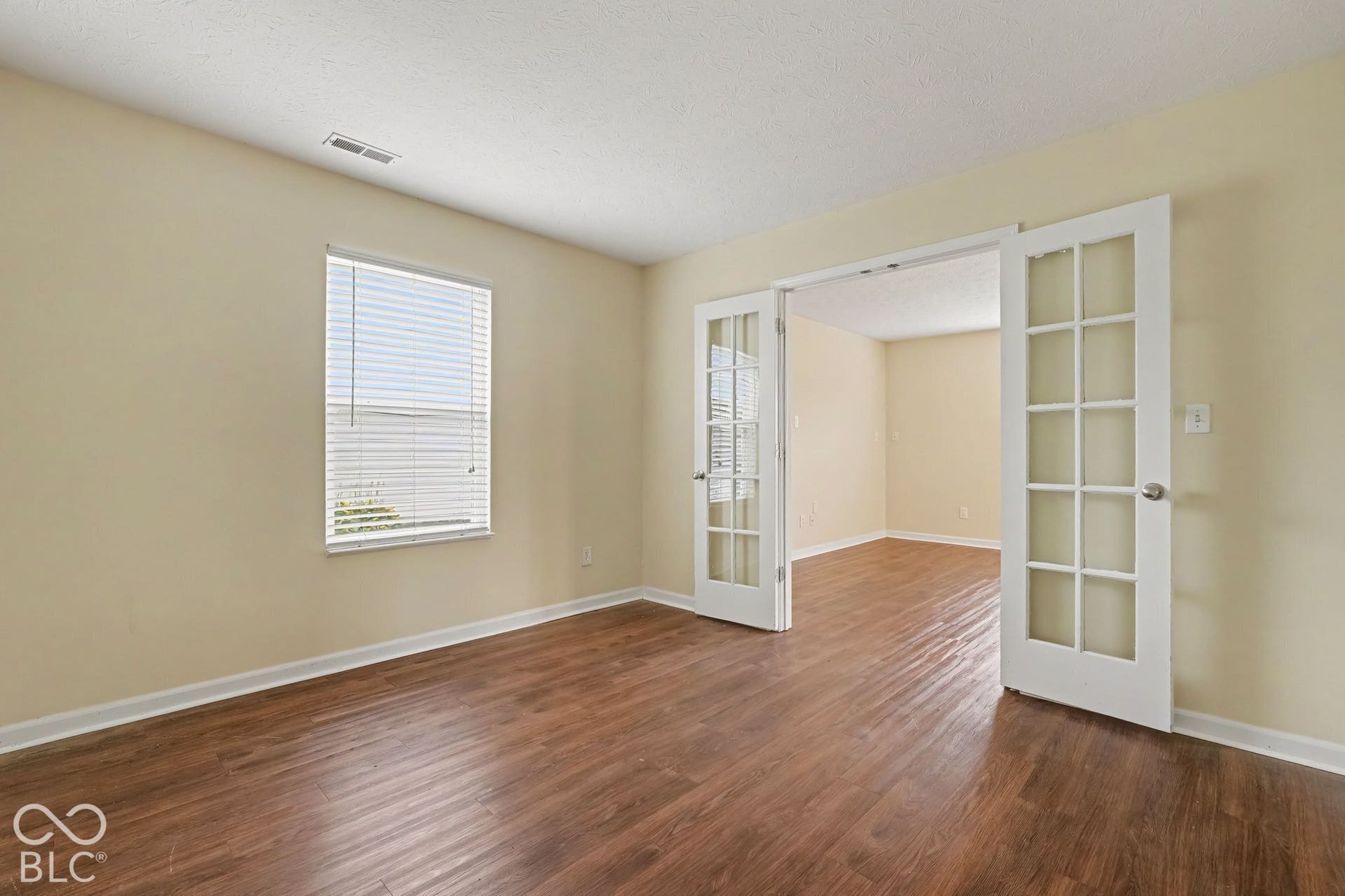 Room featuring wood-finish flooring, white French doors with glass panes, and a single window with horizontal blinds