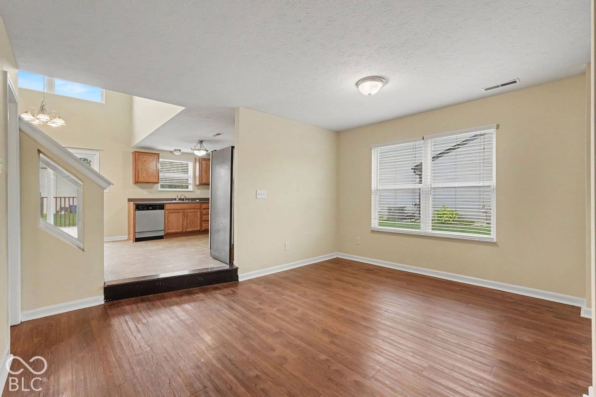 Wood-finish flooring, elevated kitchen area with wooden cabinetry, stainless steel dishwasher, and neutral wall tones
