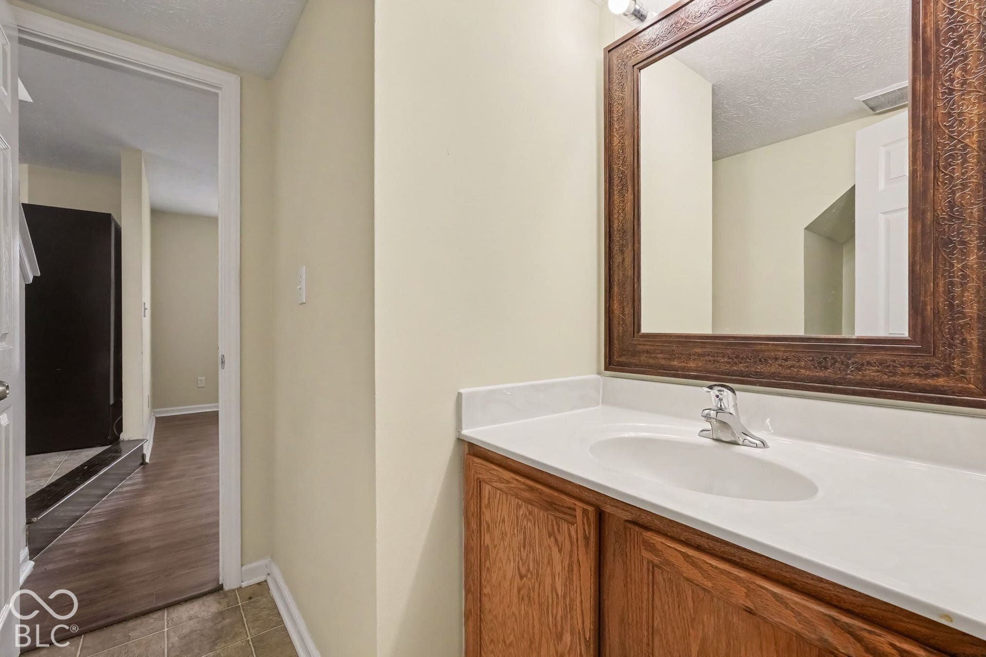 Vanity with wood-finish cabinetry, solid-surface countertop, integrated basin, chrome faucet, and decorative framed mirror