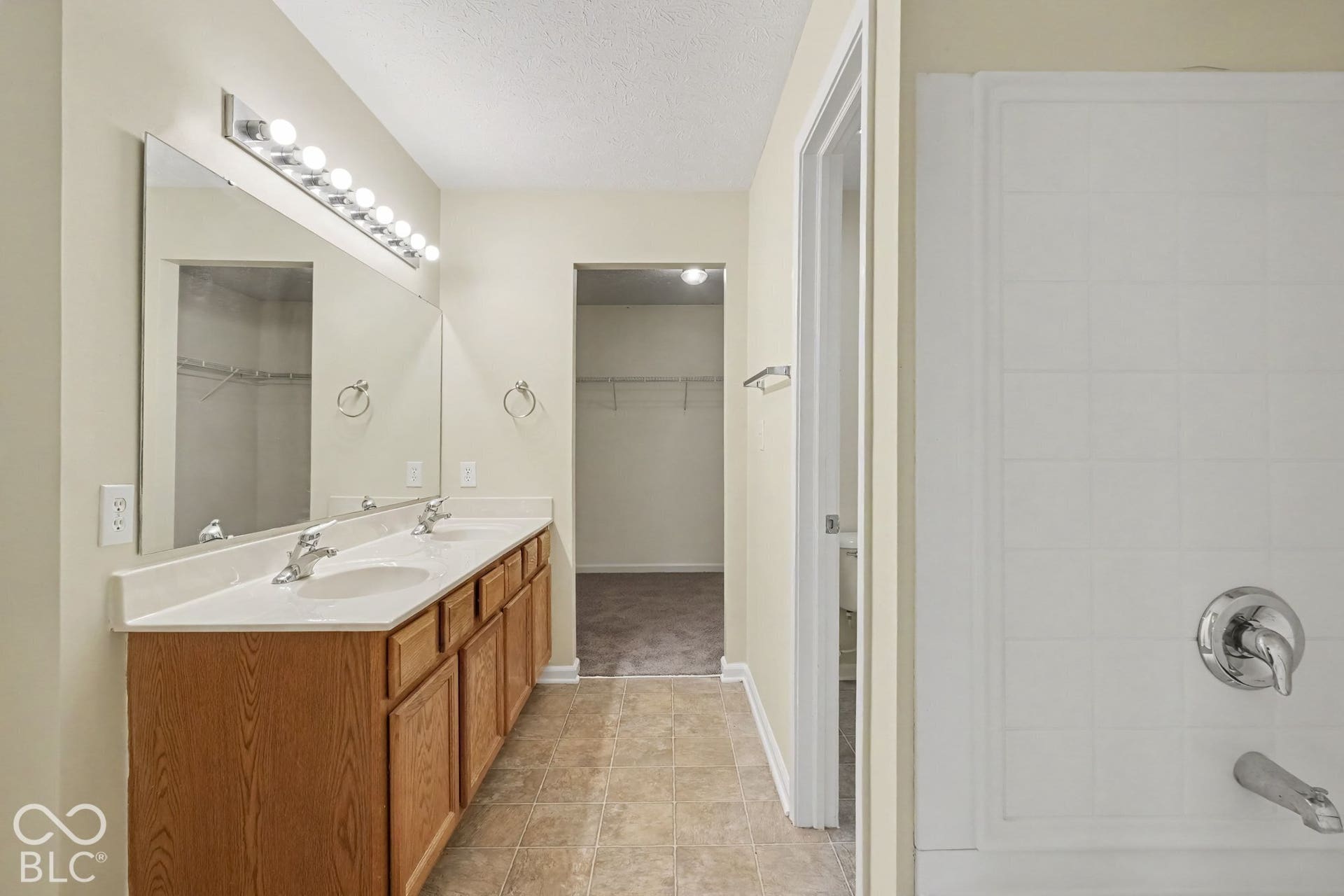 Bathroom featuring a double-sink vanity with wood-finish cabinetry, solid-surface countertop, full-width vanity mirror, tile-surround tub, and integrated storage area