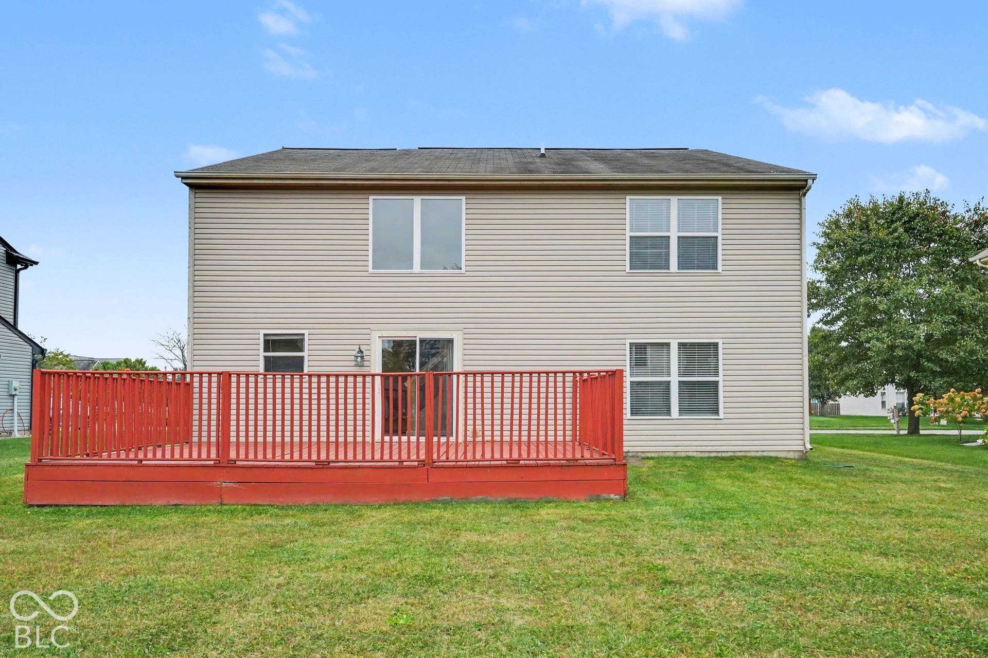 Two-story exterior with vinyl siding, shingled roof, sliding glass door, and a spacious raised wooden deck with railings