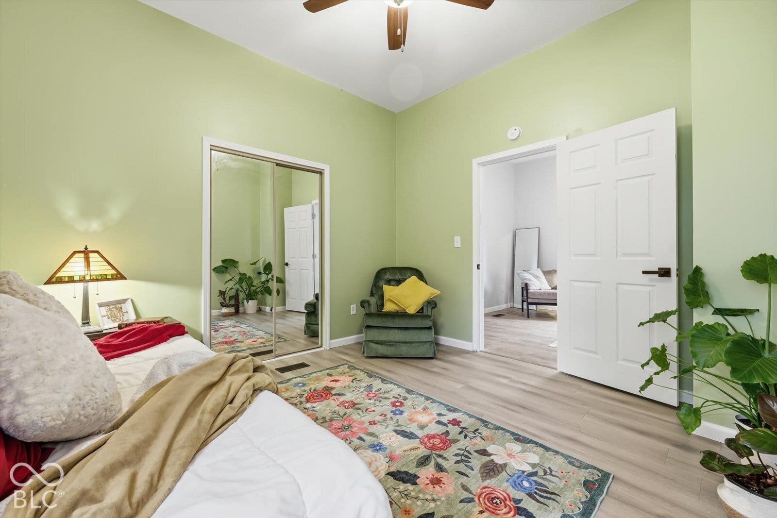 Wood-finish flooring, mirrored sliding closet doors, six-panel interior door with matte black hardware, and ceiling fan with integrated light fixture