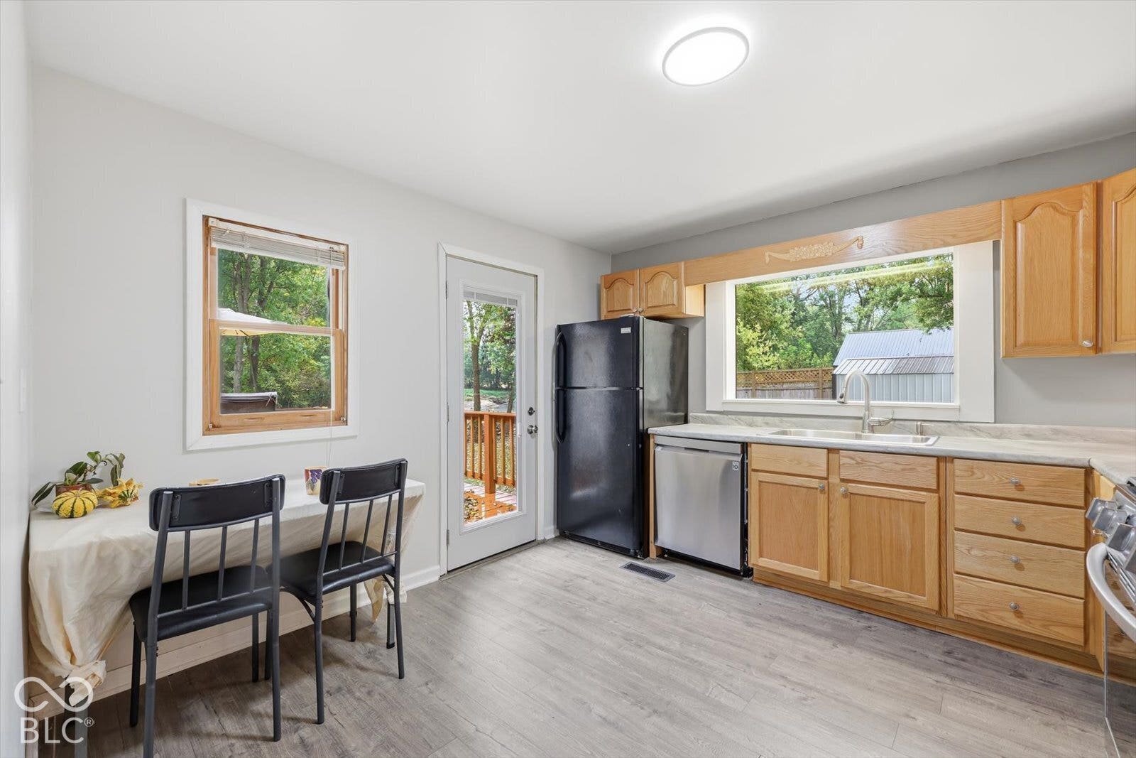 Kitchen featuring wood-finish cabinetry, neutral countertops, stainless steel dishwasher, wood-finish flooring, and a large picture window