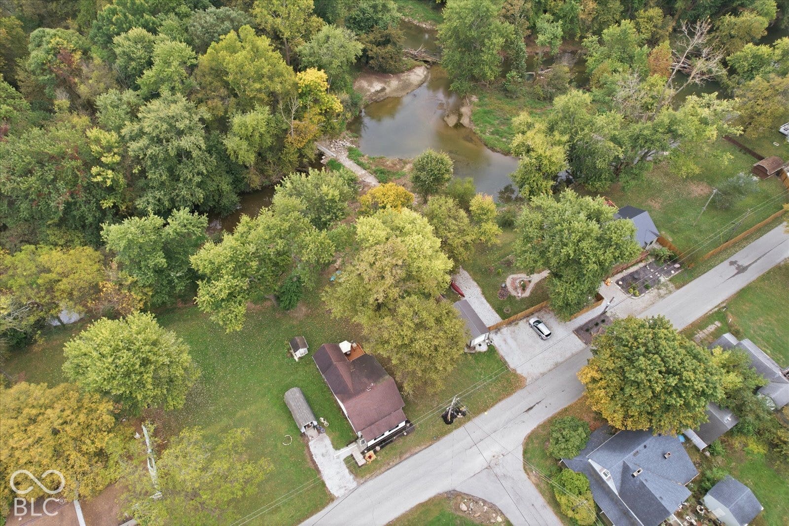 Aerial perspective of a property featuring a wooded lot, mature trees, an expansive lawn, and direct creek frontage