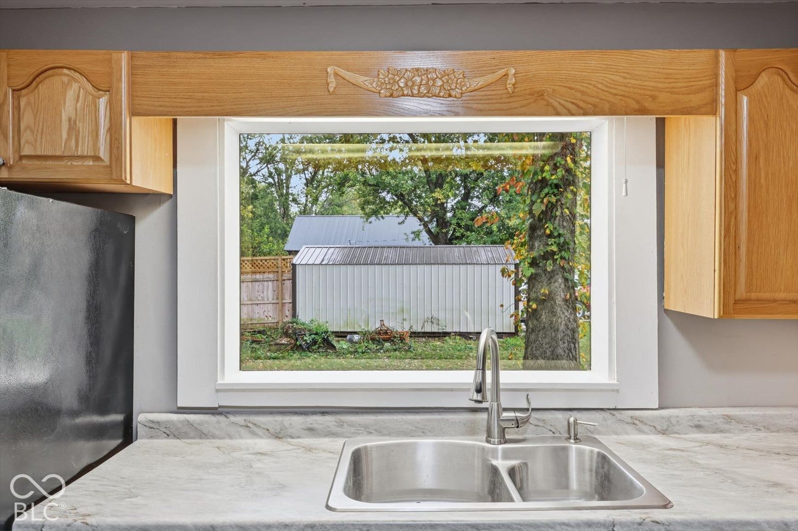Kitchen window featuring natural light, stainless steel double-basin sink, high-arc faucet, and decorative wood cabinetry valance