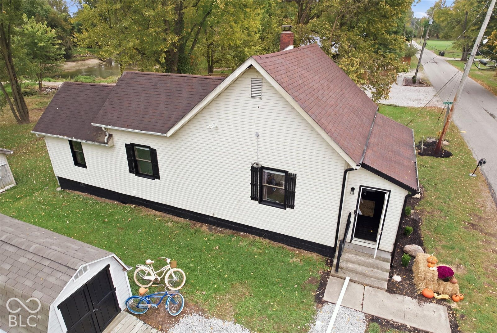 Exterior featuring light-colored horizontal siding, dark window shutters, a multi-gabled roofline, a brick chimney, and a detached outbuilding with black double doors