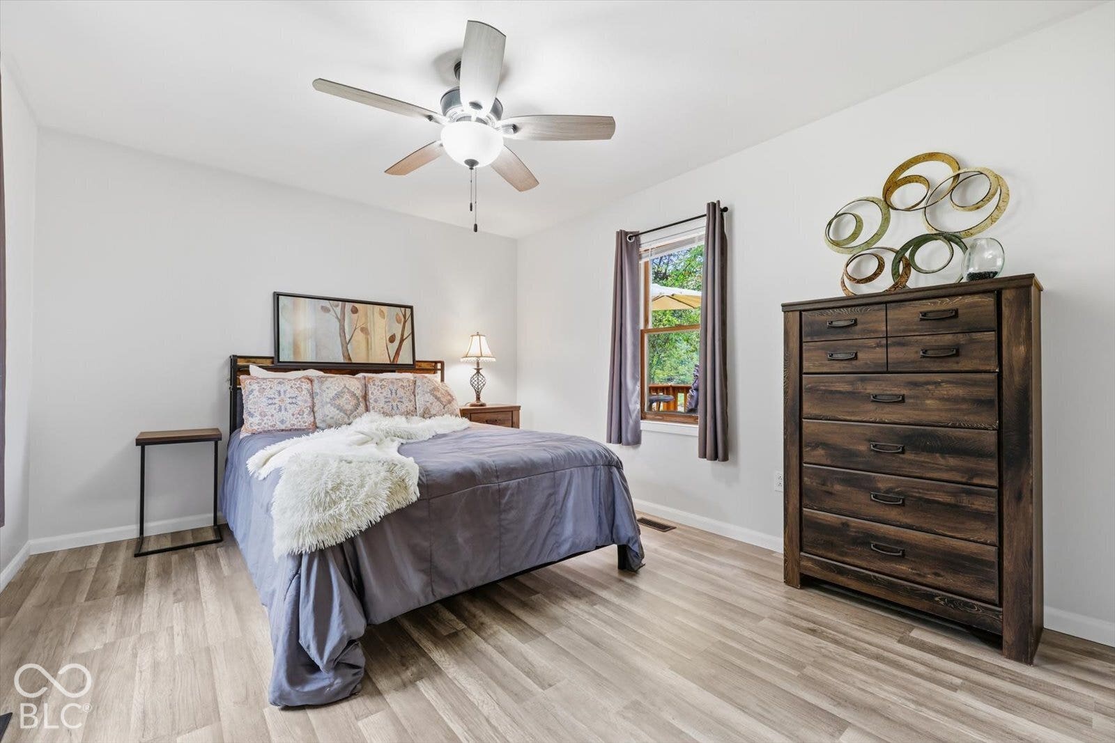 Neutral interior space featuring wood-finish flooring, a ceiling fan with integrated lighting, and a single-pane window