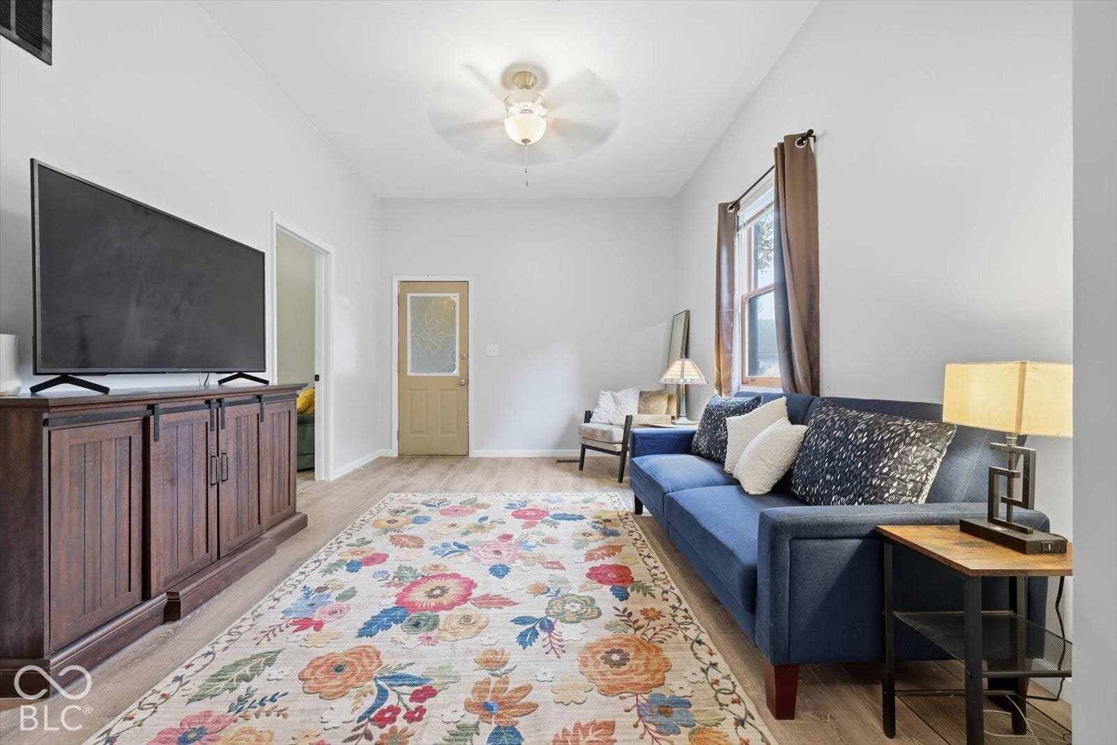 Living space featuring wood-finish flooring, a neutral color palette, ceiling fan with integrated lighting, and an exterior door with a frosted glass insert