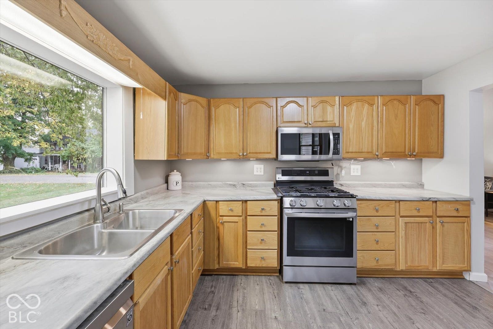 Kitchen featuring wood cabinetry, stone-finish countertops, wood-finish flooring, stainless steel gas range, and a dual-basin stainless steel sink