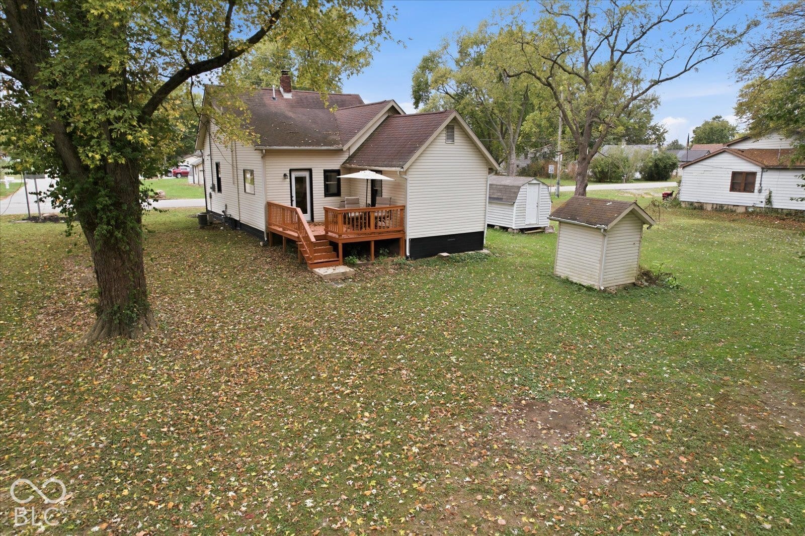 Expansive backyard featuring mature trees, a raised wood deck, and two detached storage structures