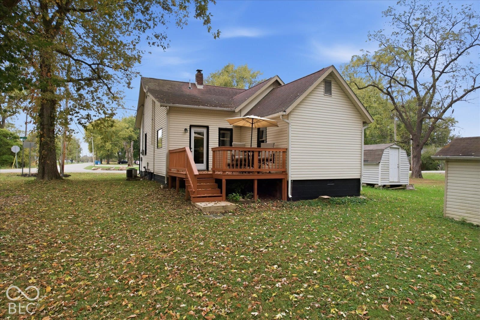 Exterior featuring light-colored siding, a raised wood deck, a chimney, and a detached storage shed situated on a spacious lot
