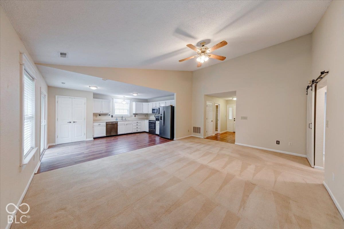 6405 Lonestar Drive, Indianapolis, IN 46237 Open-concept interior featuring vaulted ceilings, wood-finish flooring in the kitchen area, carpeted flooring, a ceiling fan with integrated lighting, and white cabinetry
