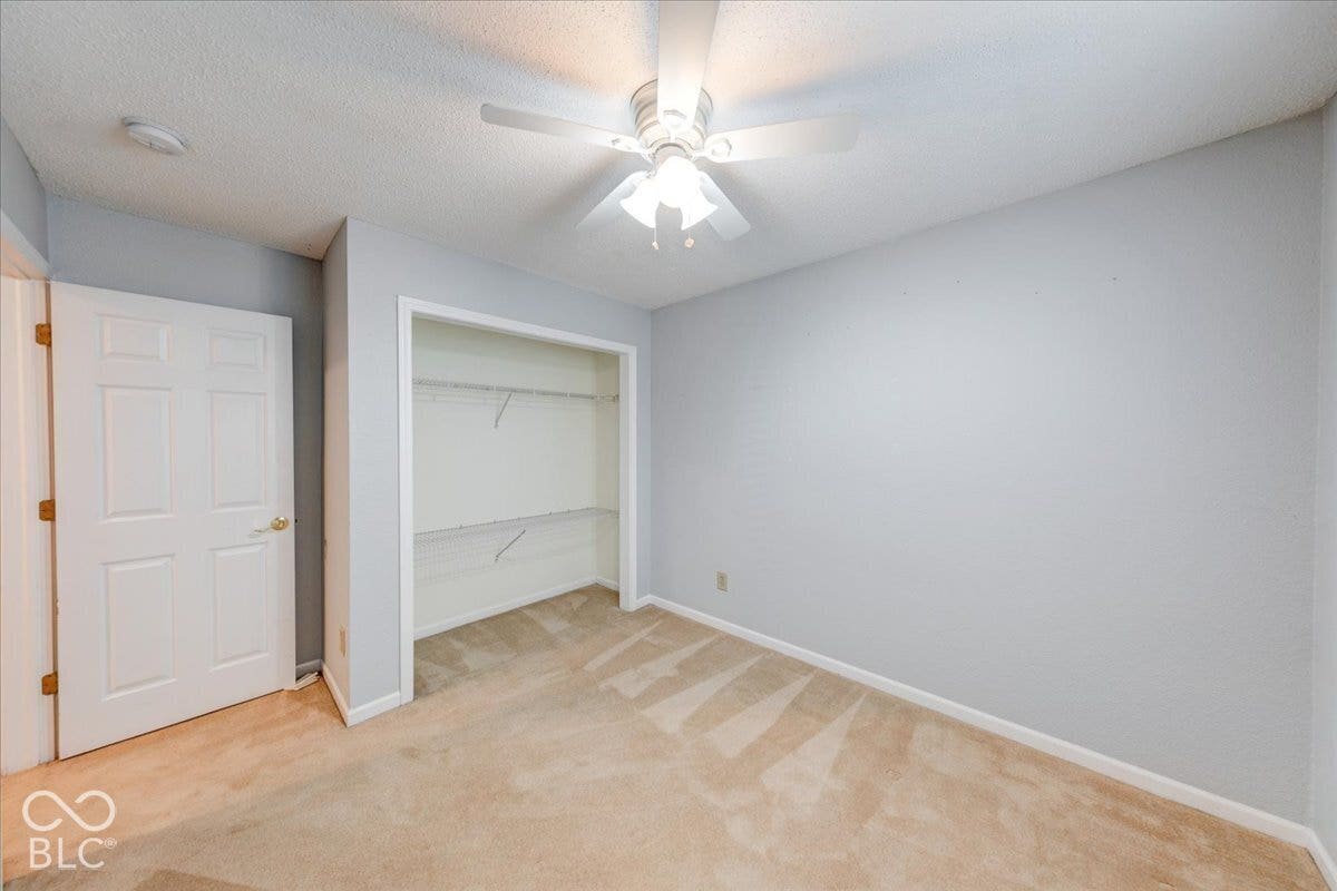 6405 Lonestar Drive, Indianapolis, IN 46237 Neutral-toned interior featuring wall-to-wall carpeting, a six-panel door, a ceiling fan with integrated lighting, and a reach-in closet with built-in shelving
