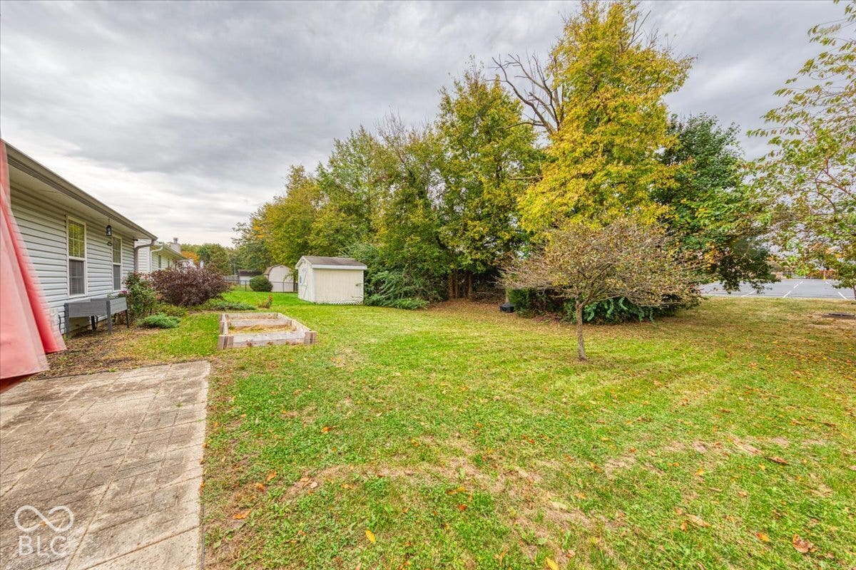 6405 Lonestar Drive, Indianapolis, IN 46237 Rear yard featuring a paved stone patio, designated garden bed, detached storage structure, and mature trees