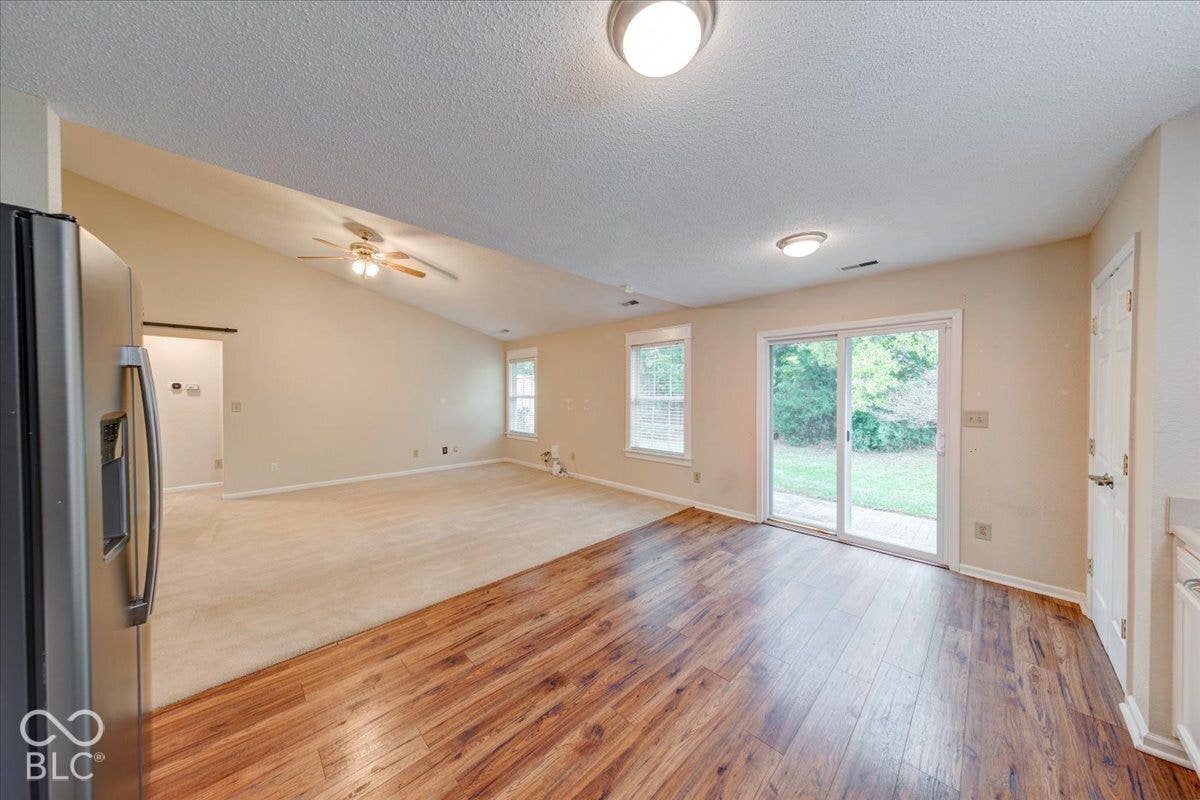 6405 Lonestar Drive, Indianapolis, IN 46237 Vaulted ceiling with integrated ceiling fan, wood-finish flooring, sliding glass patio door, and multiple windows providing natural light