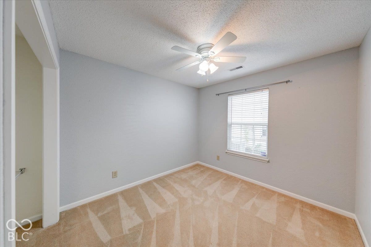 6405 Lonestar Drive, Indianapolis, IN 46237 Neutral-toned interior featuring wall-to-wall carpeting, a multi-blade ceiling fan with integrated lighting, and a single-hung window with a metal curtain rod