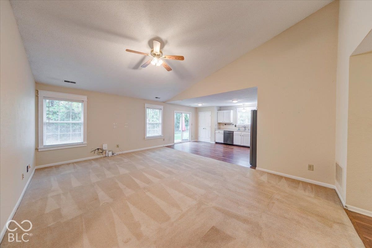 6405 Lonestar Drive, Indianapolis, IN 46237 Vaulted ceilings, carpeted flooring, multiple windows providing natural light, a ceiling fan with integrated lighting, and wood-finish flooring in the kitchen