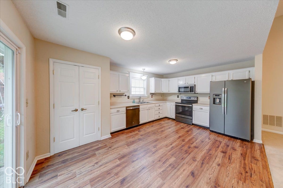 6405 Lonestar Drive, Indianapolis, IN 46237 Kitchen featuring white cabinetry, wood-finish flooring, stainless steel appliances, and sliding glass doors