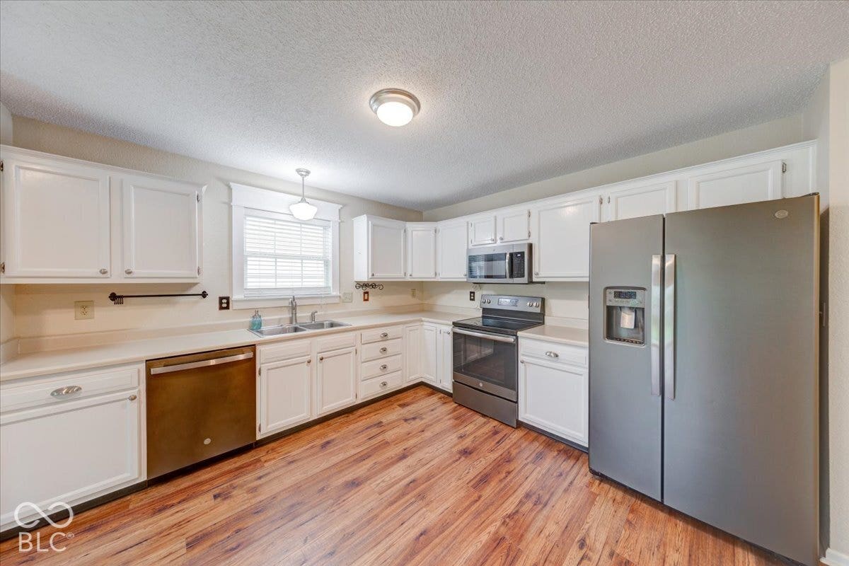 6405 Lonestar Drive, Indianapolis, IN 46237 Kitchen featuring white cabinetry, stainless steel appliances, wood-finish flooring, a double-basin sink, and recessed lighting