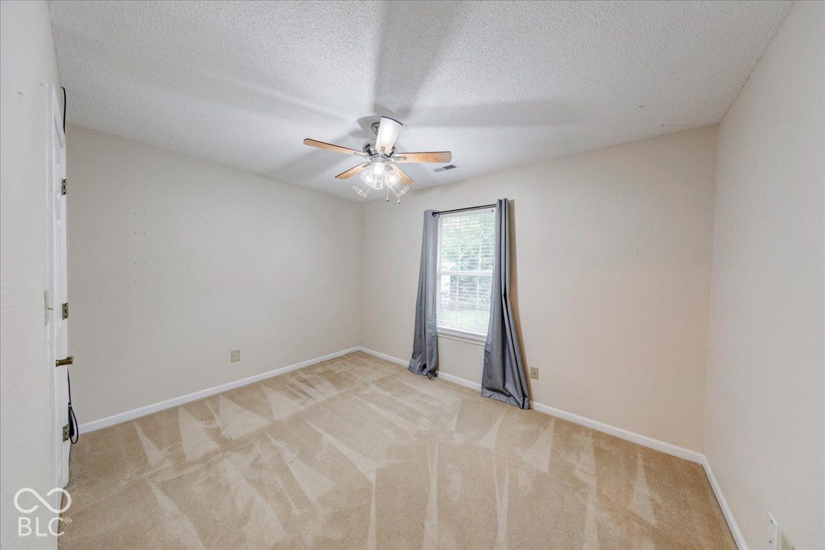 6405 Lonestar Drive, Indianapolis, IN 46237 Neutral wall tones, carpeting, ceiling fan with integrated multi-bulb light fixture, and a single-pane window