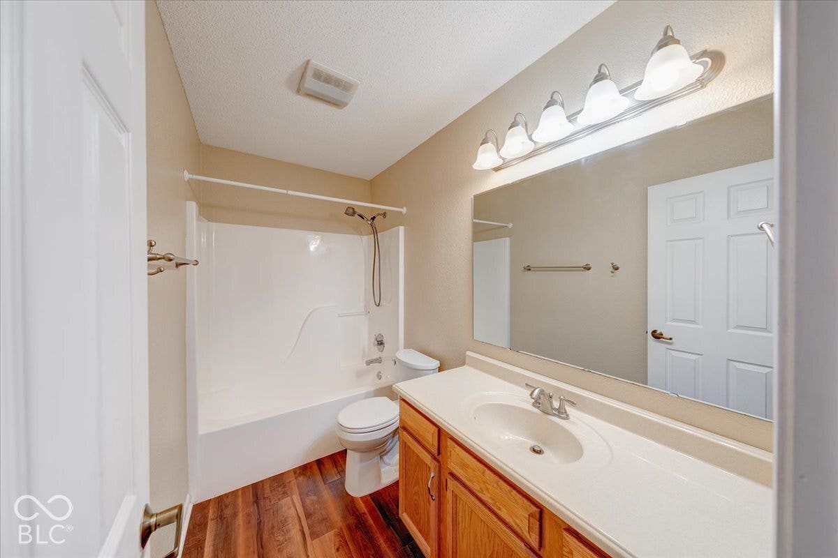 6405 Lonestar Drive, Indianapolis, IN 46237 Full-width vanity with an integrated sink, wood-finish flooring, white tub-shower combination with a handheld showerhead, and a large wall-mounted vanity mirror with a four-light fixture