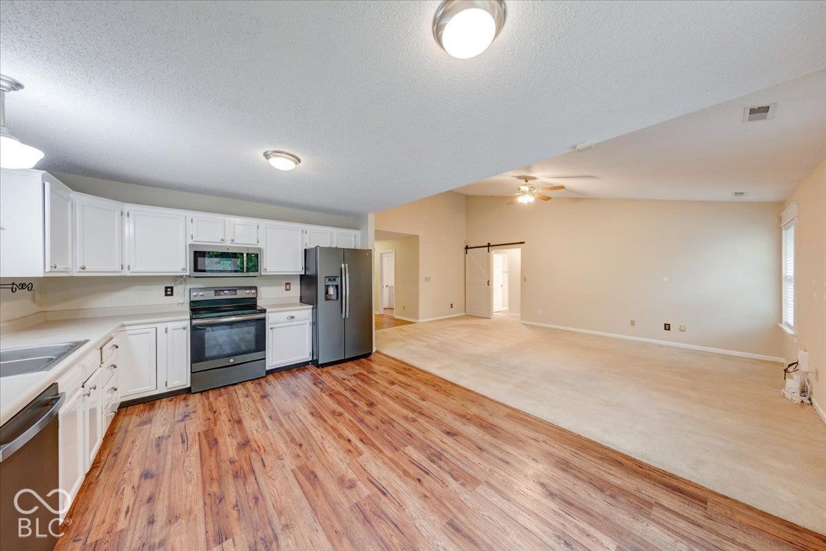 6405 Lonestar Drive, Indianapolis, IN 46237 Kitchen featuring white cabinetry, stainless steel appliances, wood-finish flooring, vaulted ceiling, and sliding barn-style door