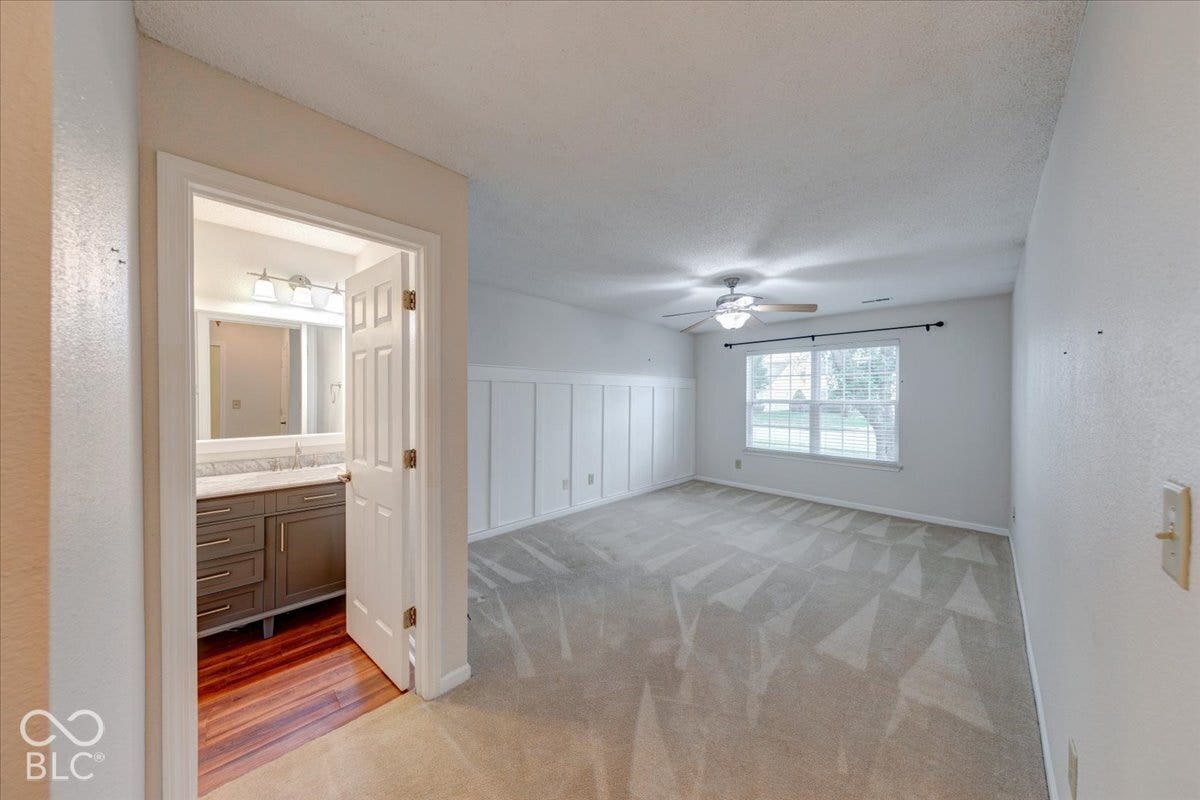 6405 Lonestar Drive, Indianapolis, IN 46237 Room featuring wainscoting, wall-to-wall carpeting, and a ceiling fan, including an entrance to a bathroom with wood-finish flooring and a vanity with a light-toned countertop