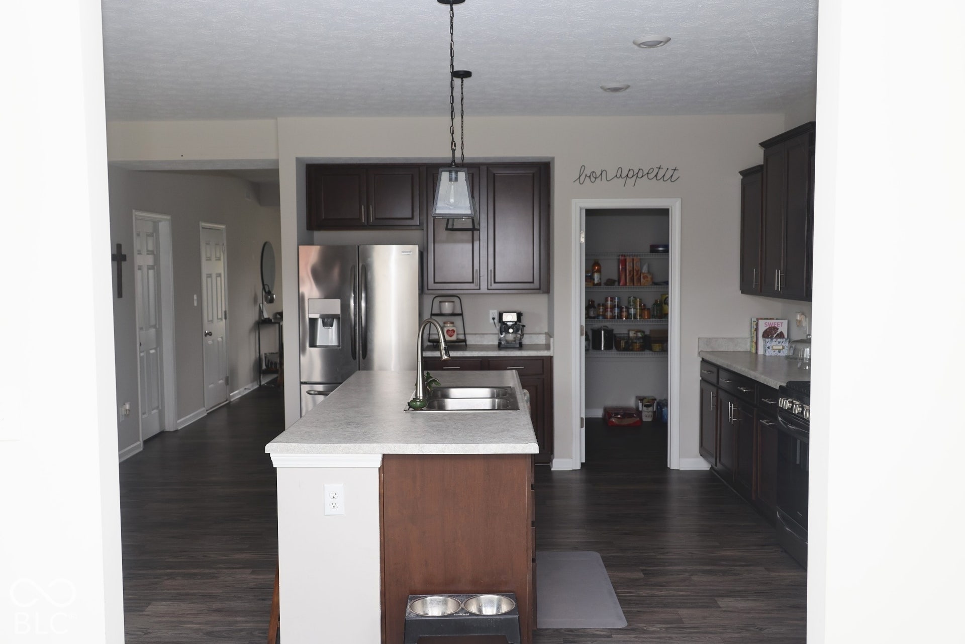 Kitchen featuring dark wood cabinetry, a central island with a double-basin sink, stone-finish countertops, stainless steel appliances, and a walk-in pantry