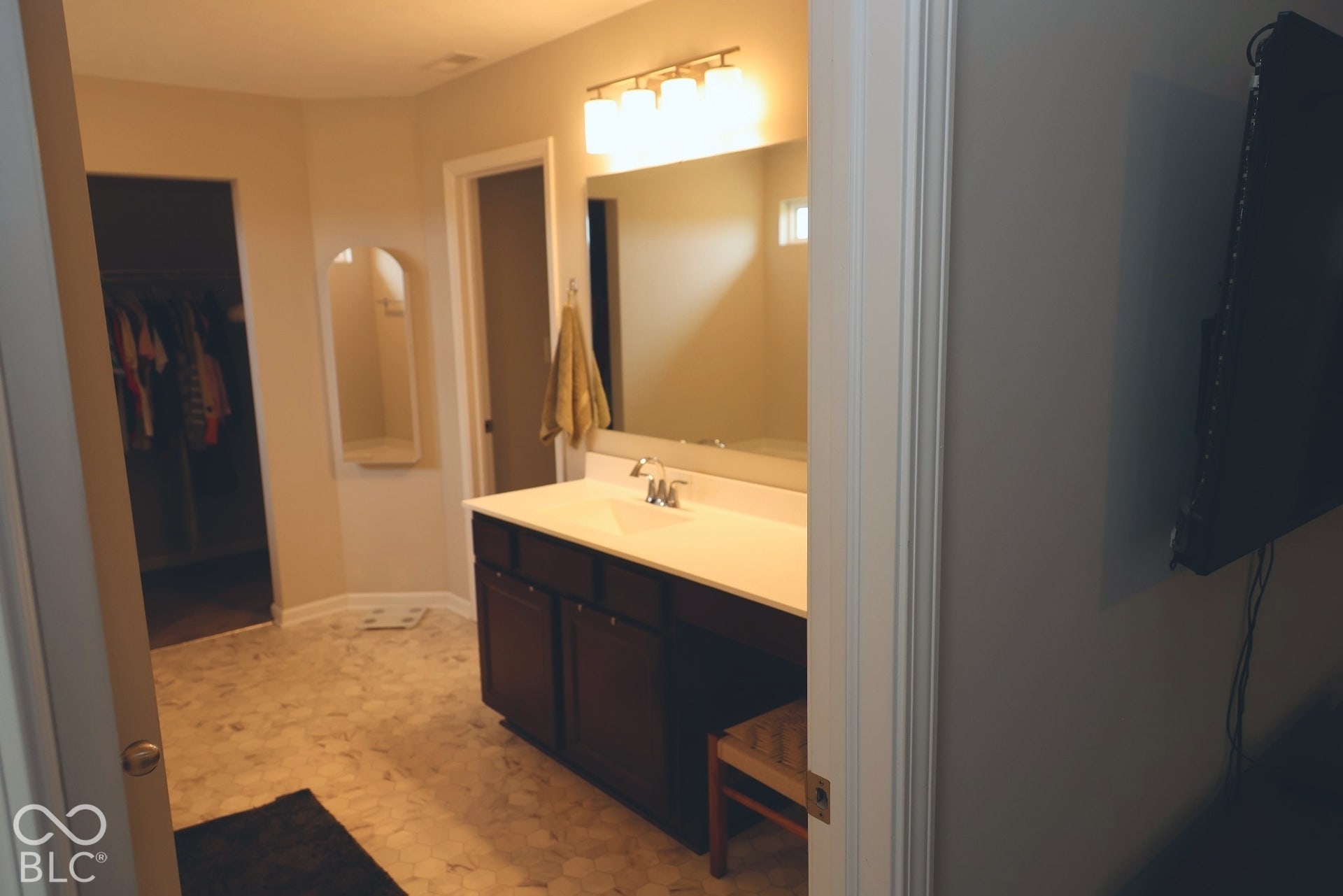Bathroom featuring dark wood-finish cabinetry, a white countertop with an integrated sink, a large wall-mounted mirror, multi-bulb vanity lighting, and patterned tile flooring