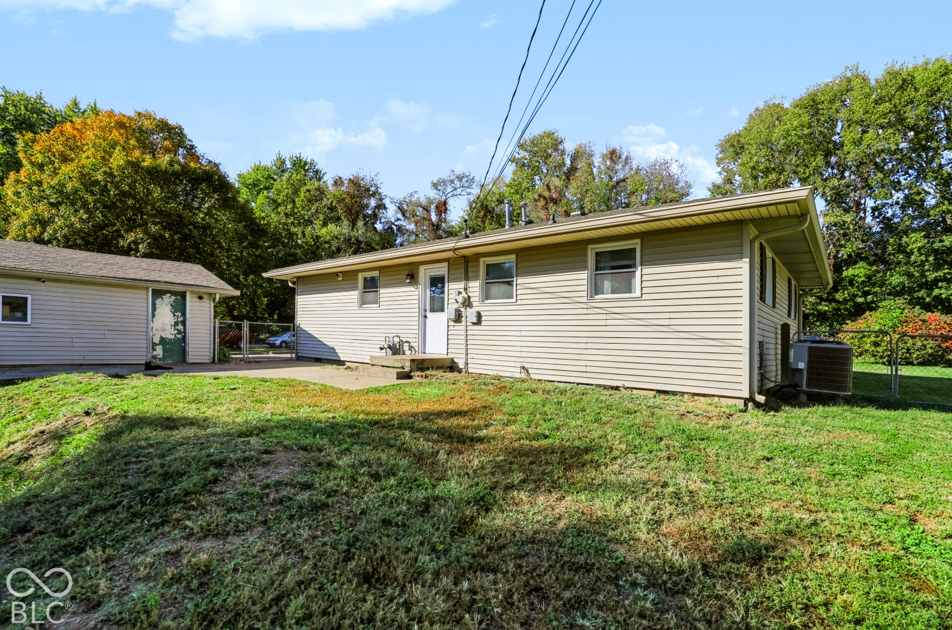 Exterior featuring vinyl siding, a detached garage, concrete patio, chain-link fencing, and mature trees