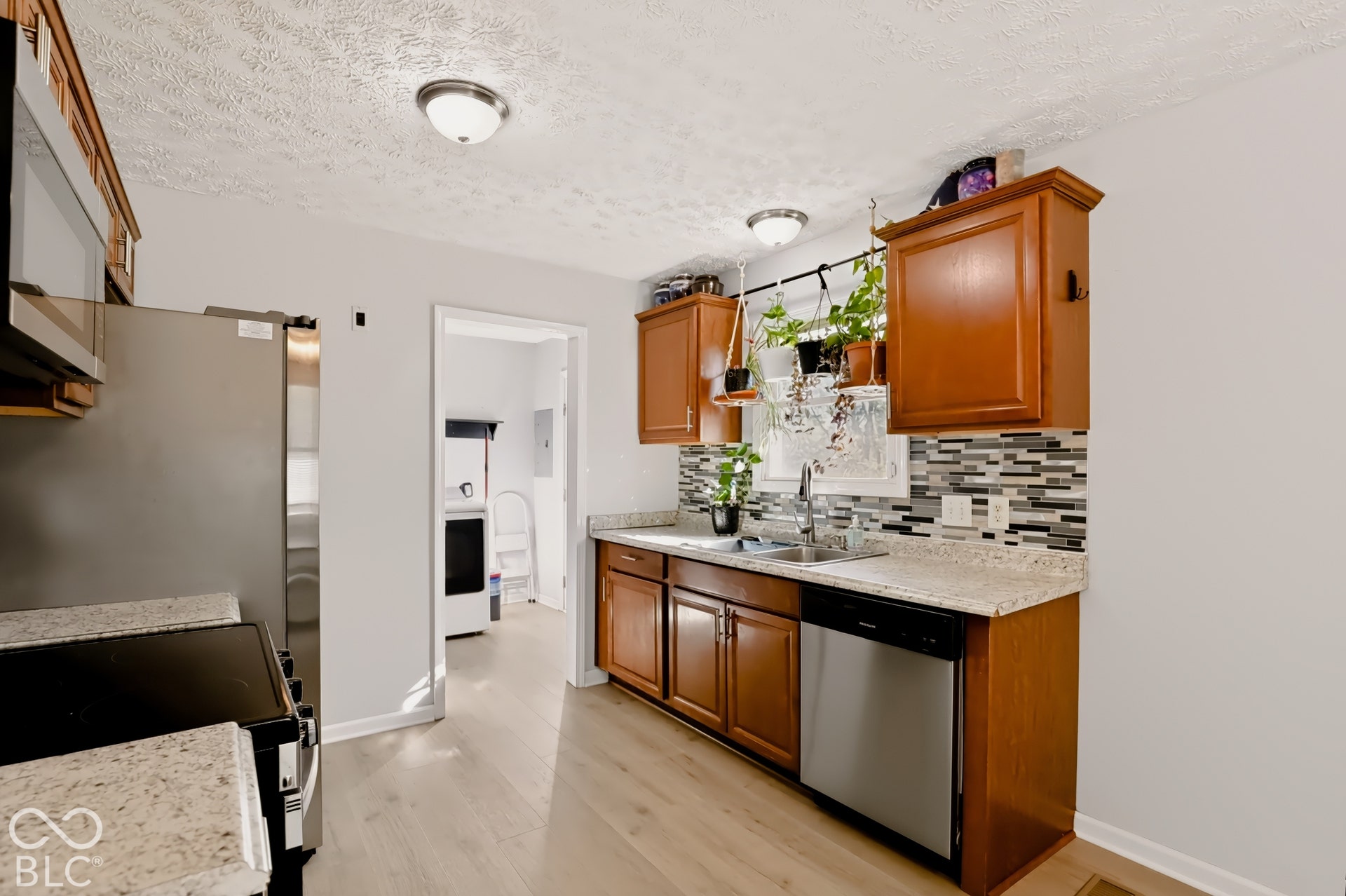 Kitchen featuring wood cabinetry, stone-finish countertops, stainless steel appliances, multi-tonal mosaic tile backsplash, and wood-finish flooring