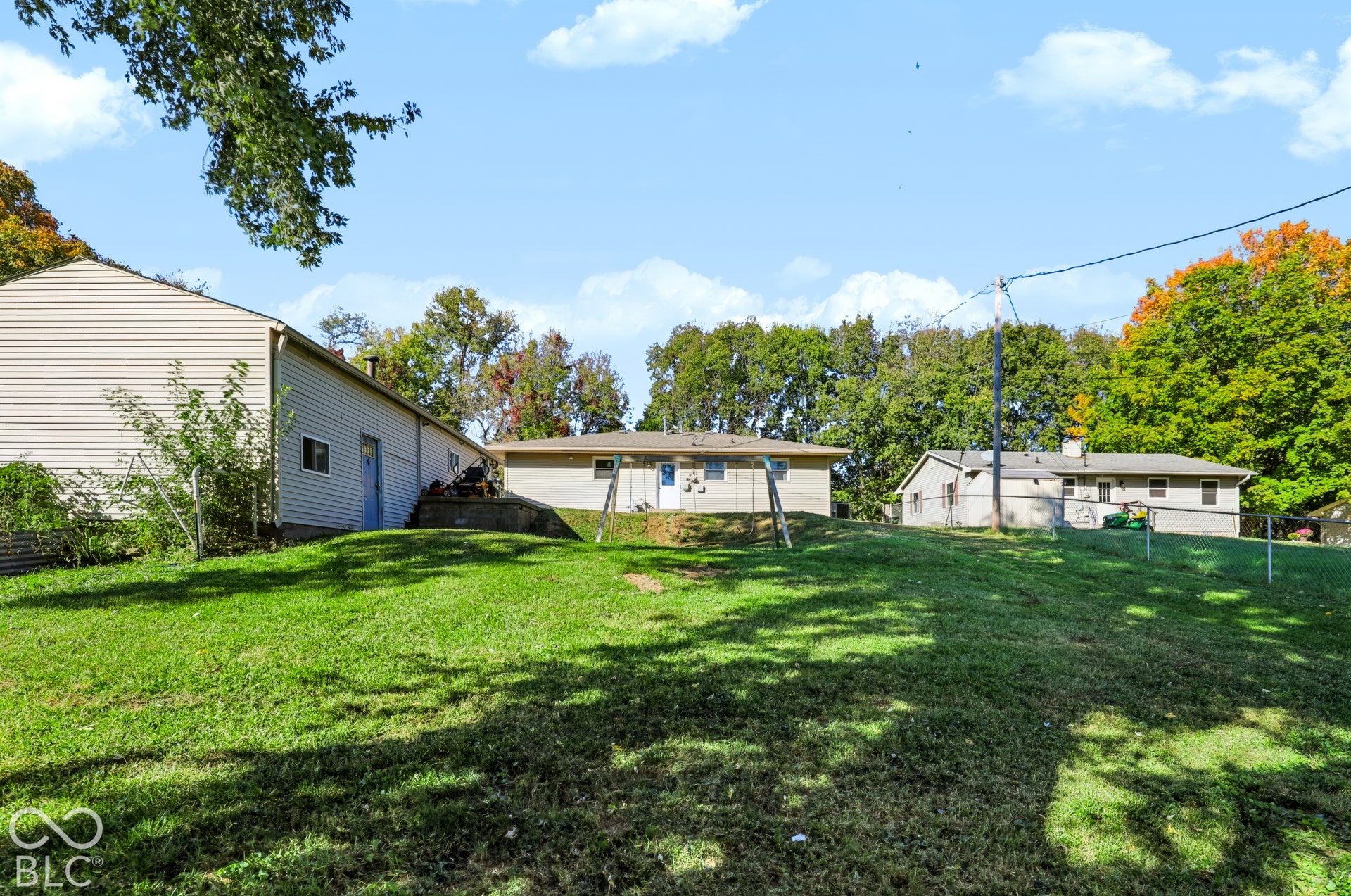 Expansive backyard featuring a sprawling lawn, mature trees, and perimeter chain-link fencing