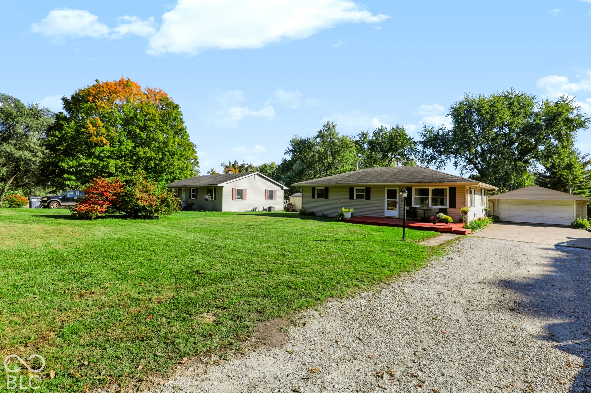 Ranch-style residence featuring light-toned siding, a low-pitched roof, an expansive open lawn, an attached garage, and a gravel driveway