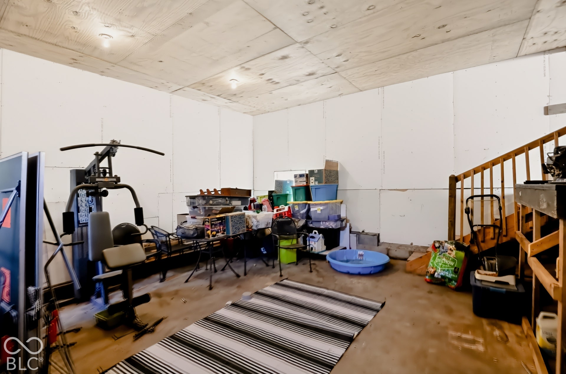 Unfinished space with plywood ceiling paneling, exposed drywall wall panels, and a wooden staircase
