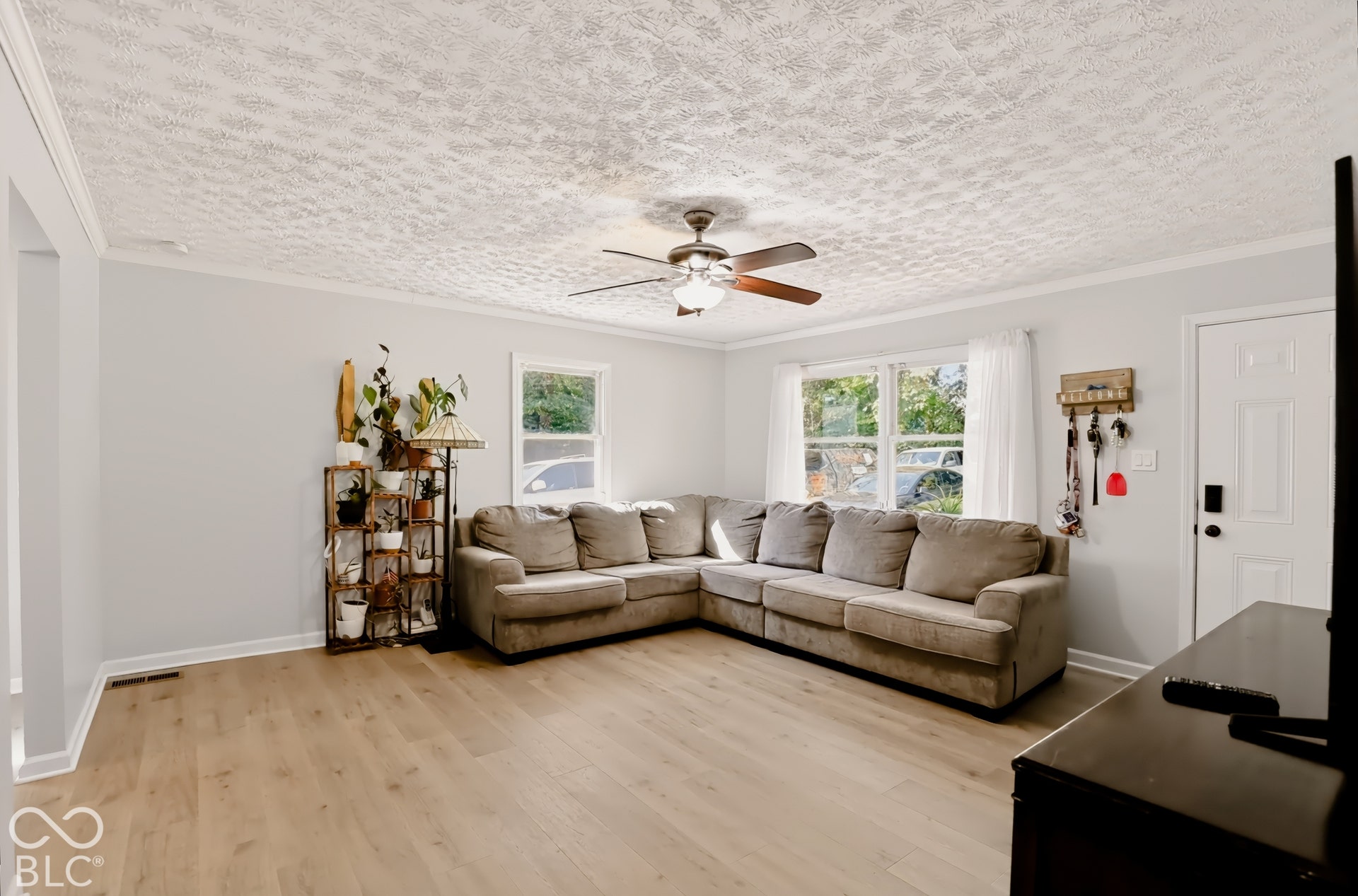 Living area featuring wood-finish flooring, textured ceiling, multiple windows, and a ceiling fan